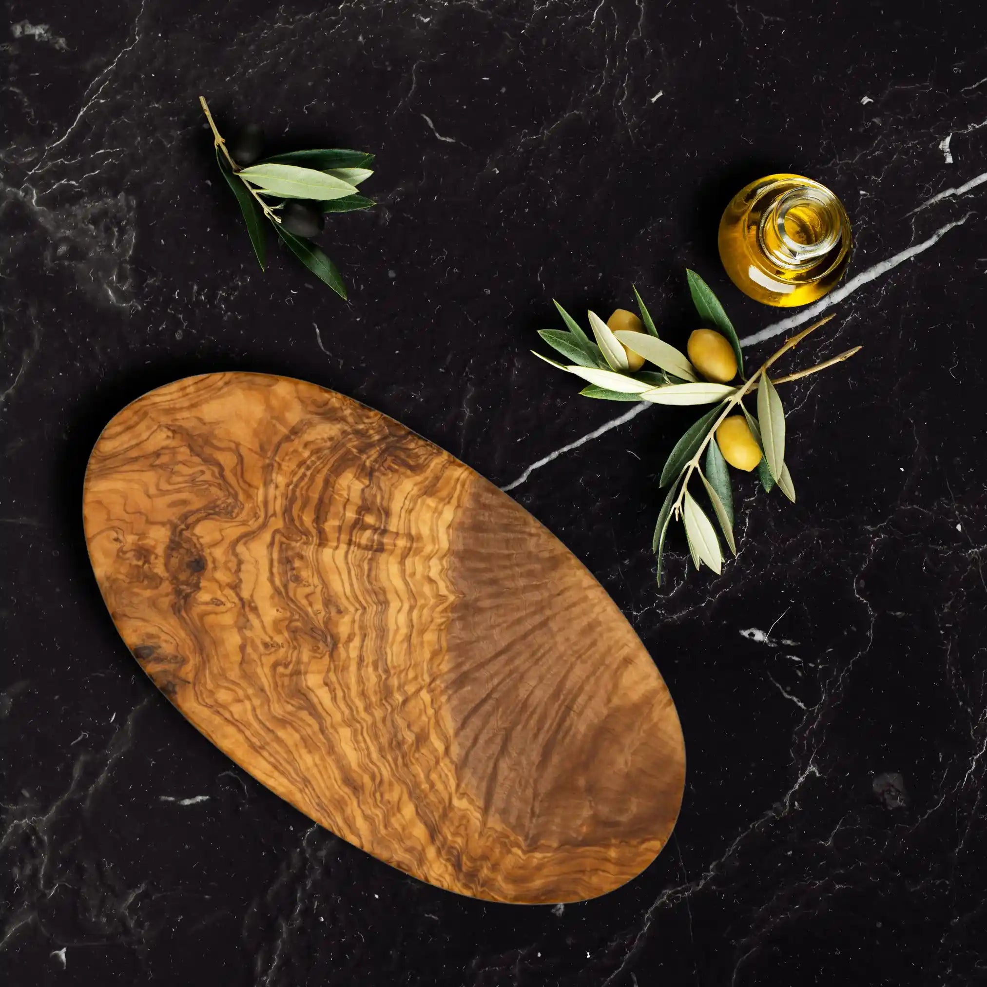 The rustic oval olive serving board is placed on a luxury dinning table.