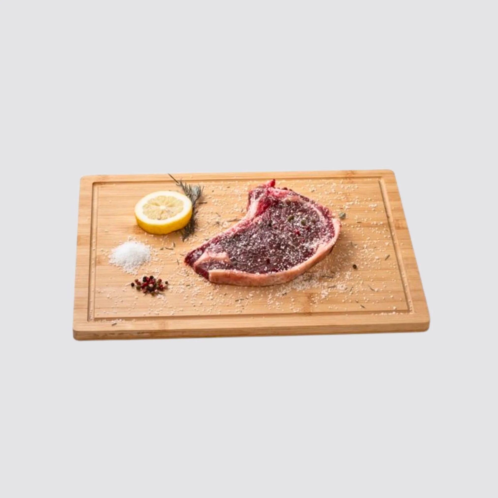 Bamboo cutting board styled with steak, herbs, lemon and salt, highlighting its versatility and suitability for kitchen use.