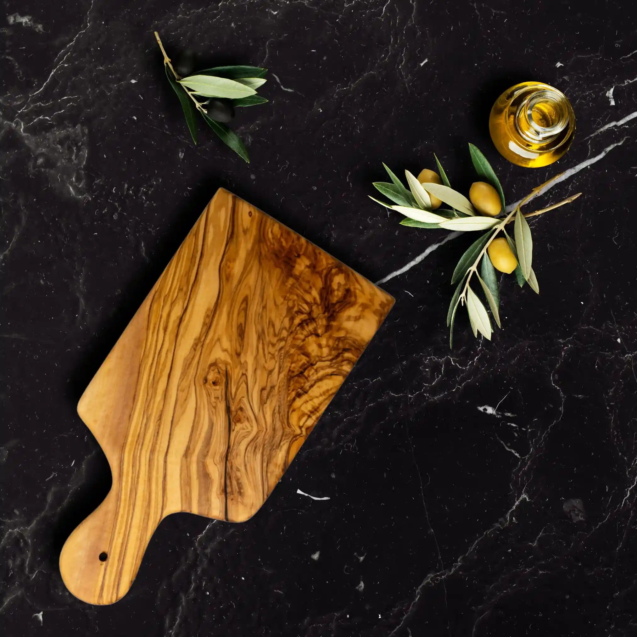An olive cutting board styled elegantly on a luxury dinning table next to green olives.