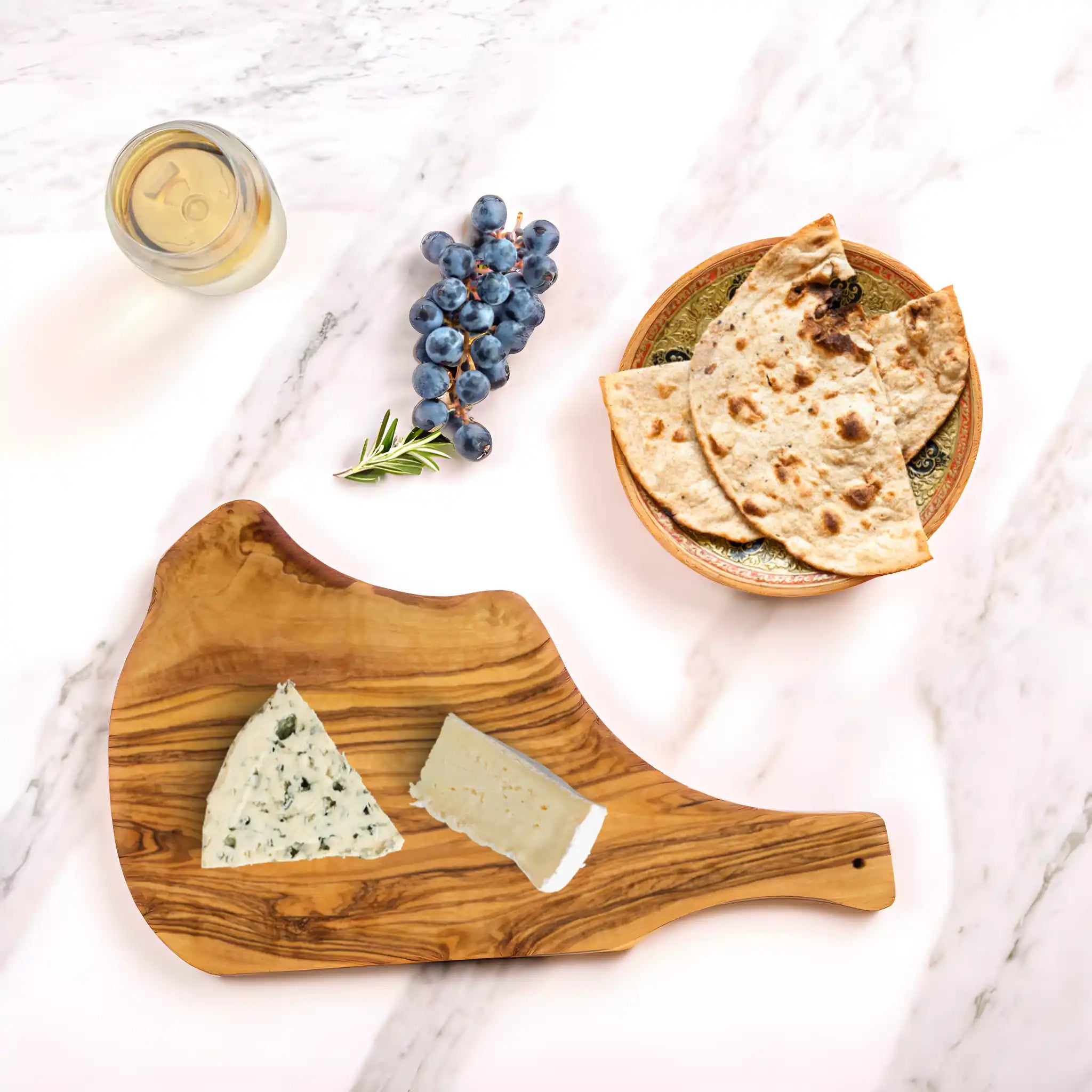 Olive wood serving board placed on a marble luxury table in a modern kitchen setting, showcasing its natural grain and rustic elegance.