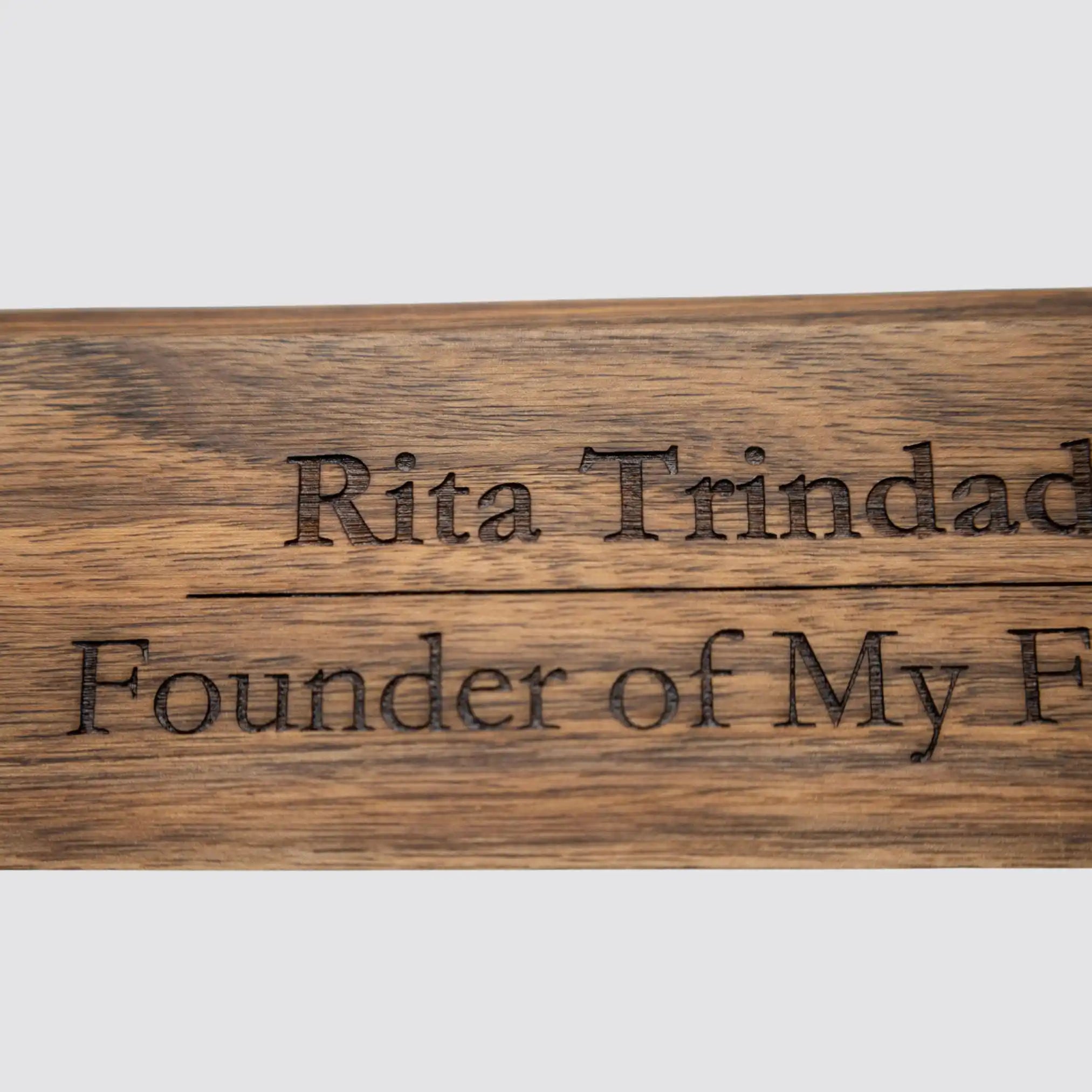 Close-up of the custom engraving on a walnut desk name plate, emphasizing the precision craftsmanship and rich wood texture on a plain white background.