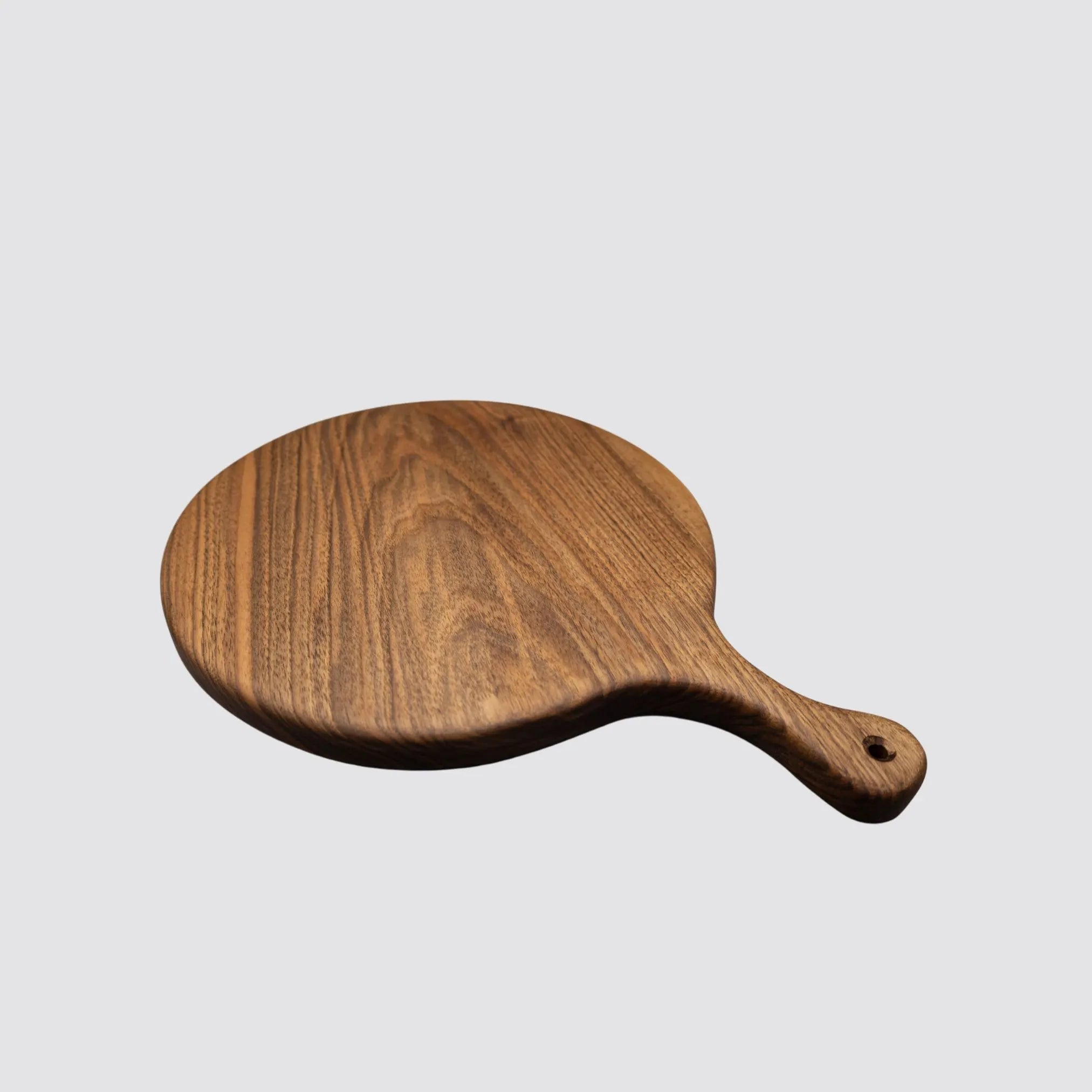 Angled view of a premium round walnut serving board, perfect for creating stunning charcuterie and cheese platters.