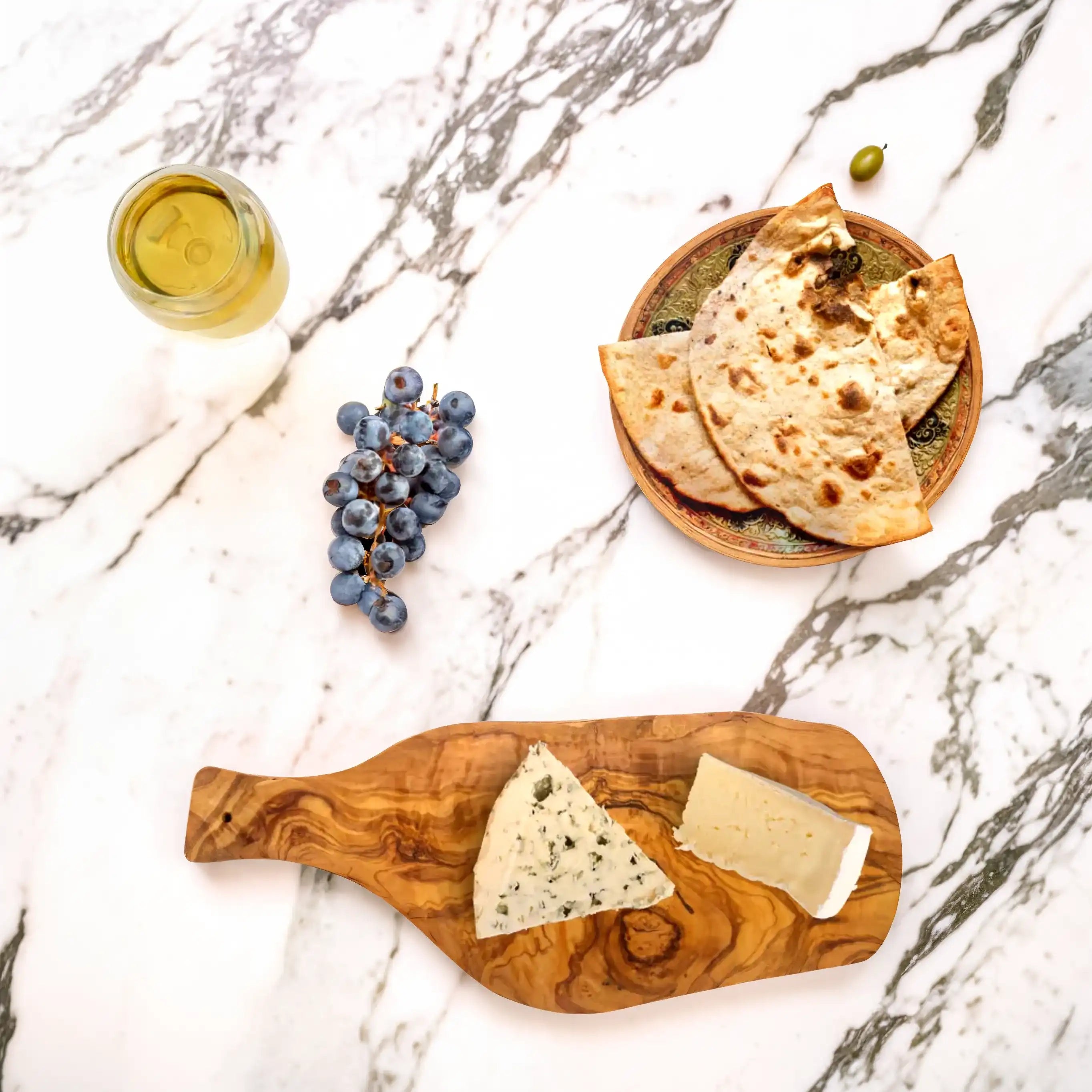 Rustic olive wood serving board styled with cheese, fresh bread, and a glass of wine, highlighting its natural grain and warm tones in a minimalist and elegant dining setup.