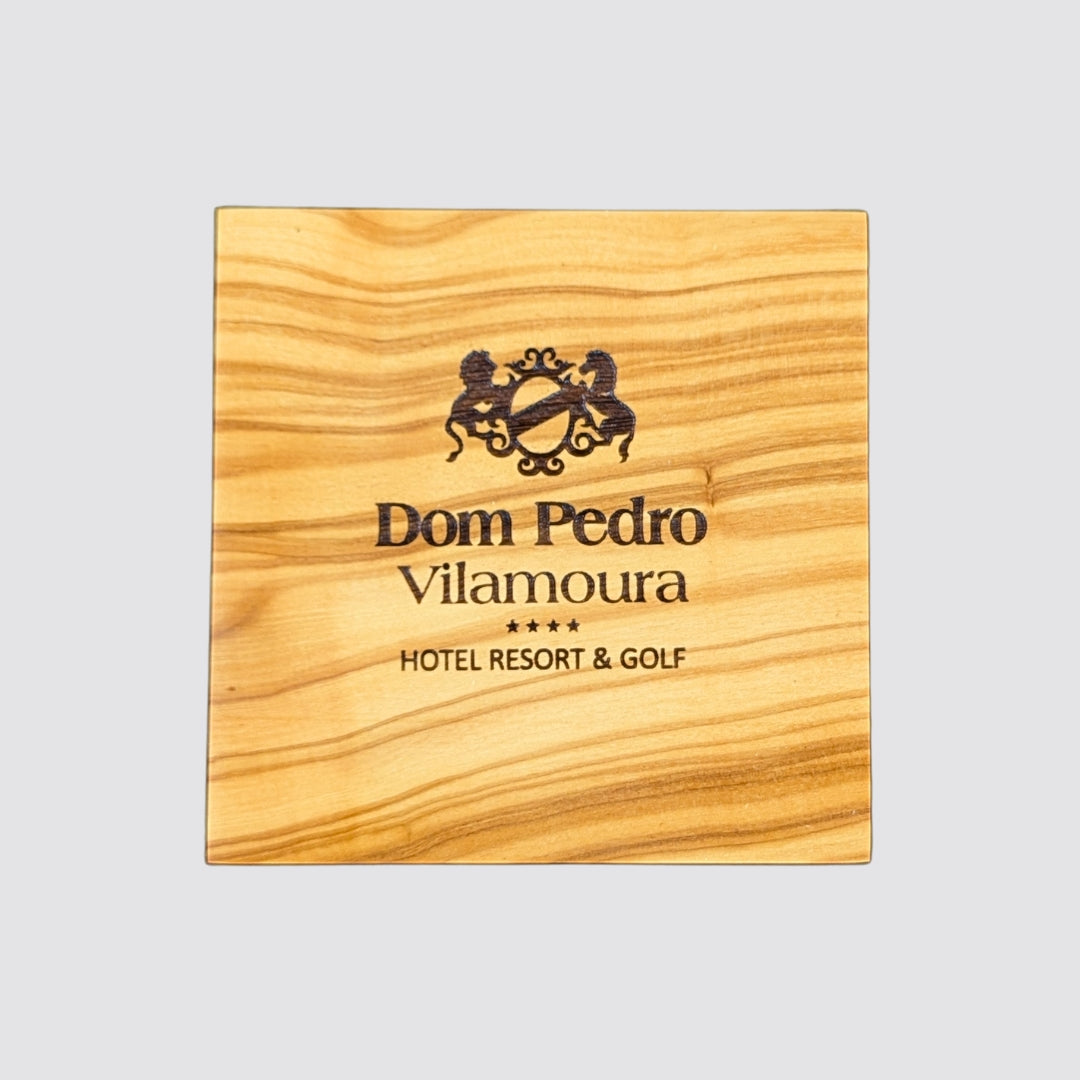 Wooden coaster with Dom Pedro Vilamoura logo and text on a light gray background